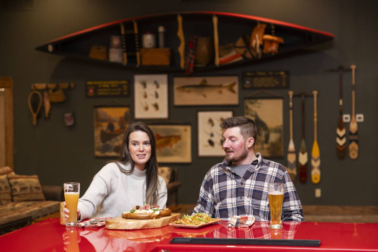 A man and woman enjoy drinks and food at a lodge bar. 